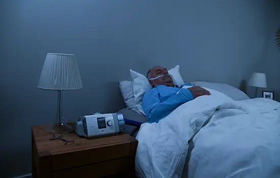 Homem dormindo com uma máquina Resmed na cabeceira da cama.