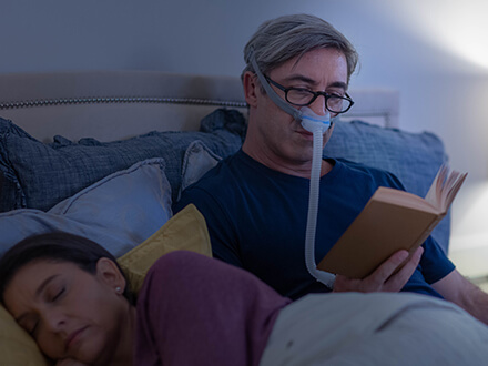 Paciente beneficia da terapia enquanto lê um livro, na cama, usando a máscara nasal minimalista AirFit N30 da ResMed