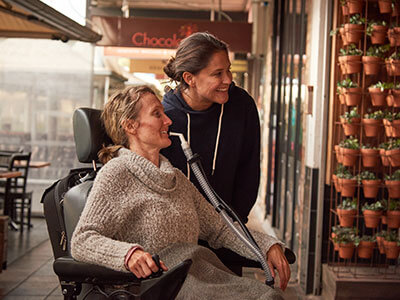 Paciente numa cadeira de rodas conectada a um dispositivo médico acompanhada por mulher