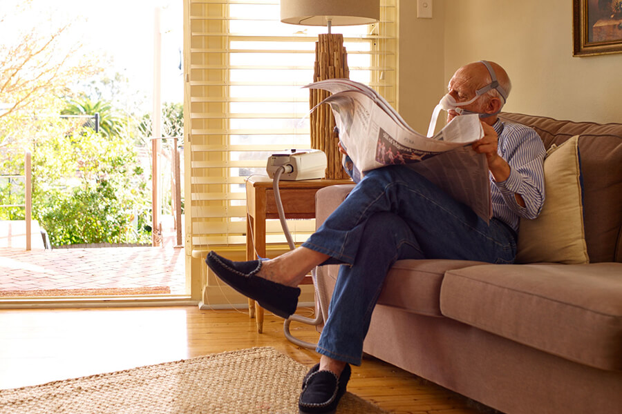 Paciente sentado a um sofá, conectado a um dispositivo, lê um jornal