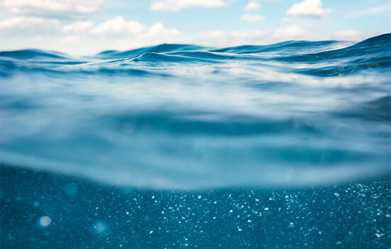 Fotografia das ondas do oceano com céu azul, tirada de dentro da água